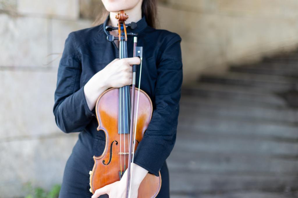 A woman holds her violin and bow protectively.