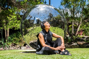 Australia Day Honours. Woman of Asian appearance in sleeveless top sits in front of a bubble like sculpture outdoors looking up toward the sky.