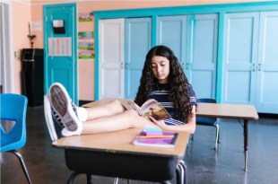 Girl reading book in classroom with feet up on desk