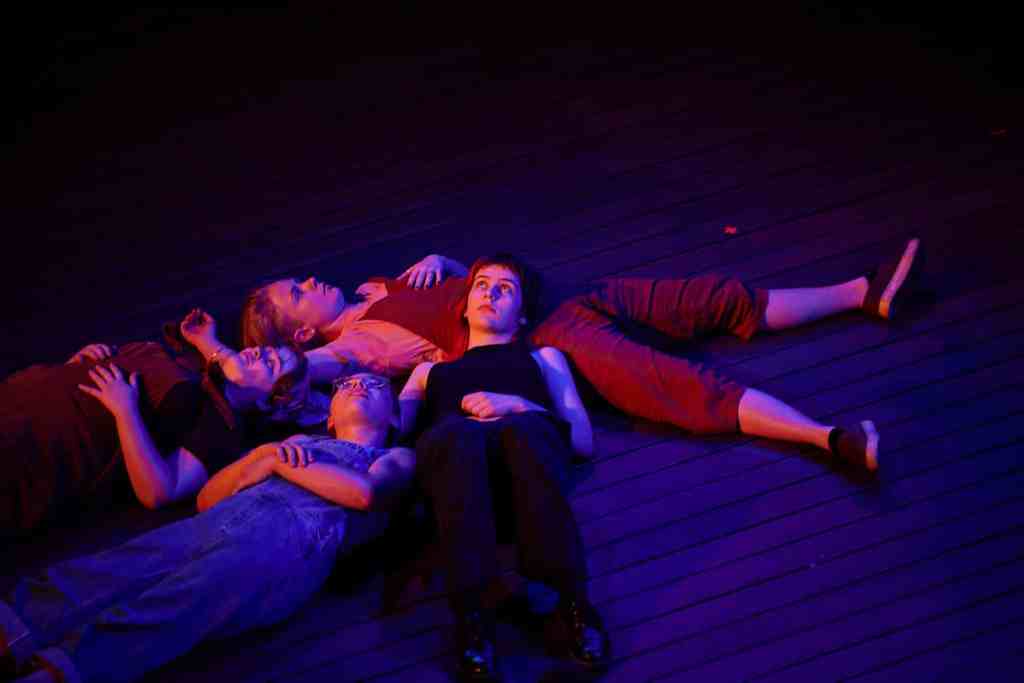 Four young women lie in an intimate heap on stage.