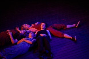 Four young women lie in an intimate heap on stage.