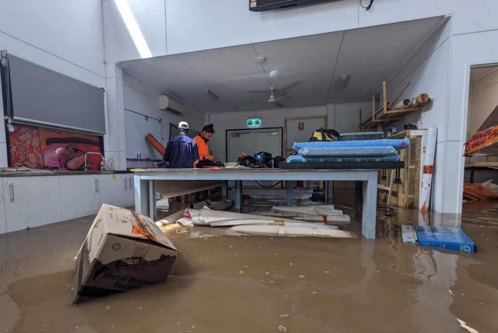 an art studio flooded to knee height with artworks and boxes floating in the water.
