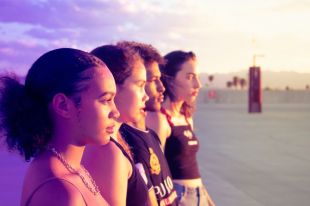 profile view of four teenagers standing outside looking towards the horizon against an open sky.