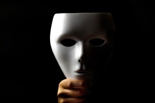 hand holding theatrical mask against a black background