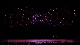 hundreds of lights appearing in the night sky over the ocean in a patterned display.
