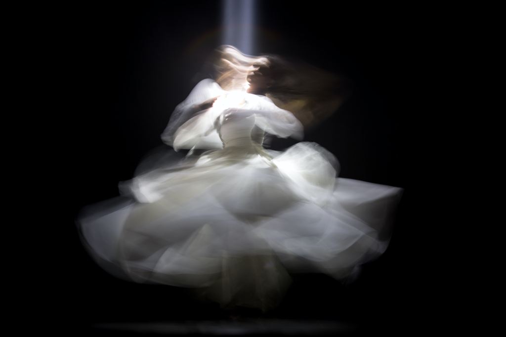 A blurred photo of a spinning dancer wearing white clothing against a black background.