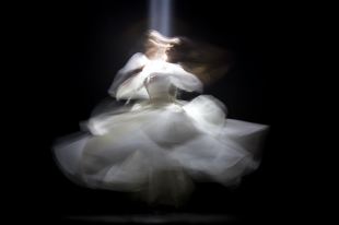 A blurred photo of a spinning dancer wearing white clothing against a black background.