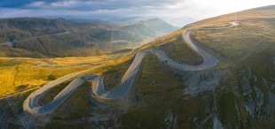 Aerial panoramic view of amazing curved road through the mountains in Romania at sunrise