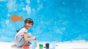 5-year-old Asian girl smiling while painting a wall mural.