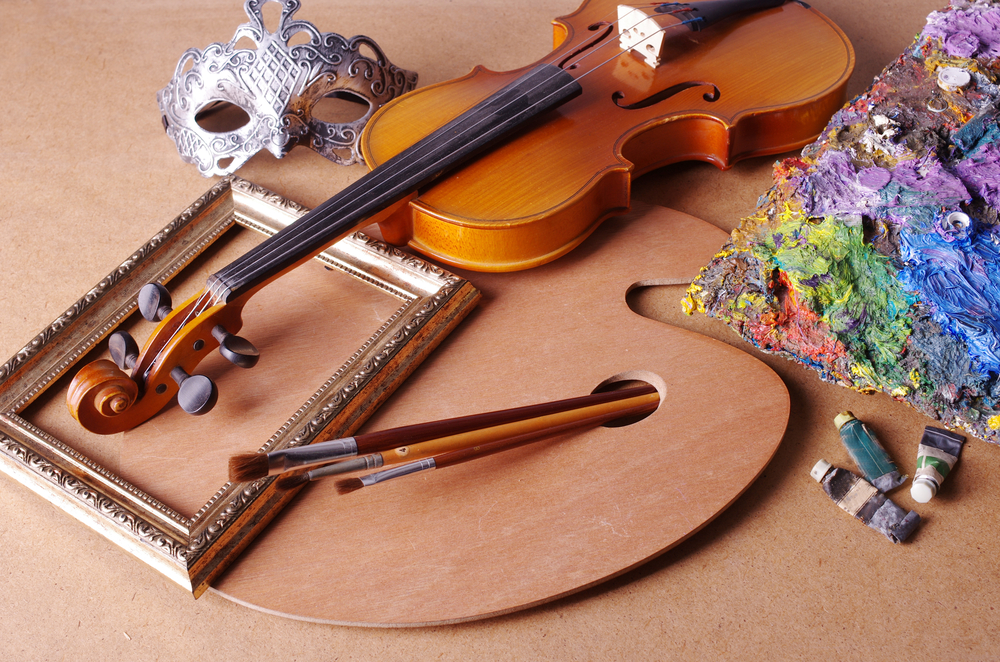 A violin, a theatrical mask, paint brushes and a paint-spattered palette arranged in an attractive group.