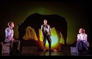 three actors on stage in front of a large filmed projection of a horse against the sun.