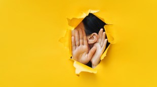 Hands held around ear to hear, with yellow background