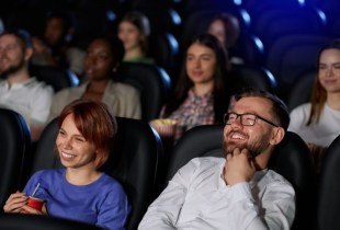 Audience members in a dark theater laughing at