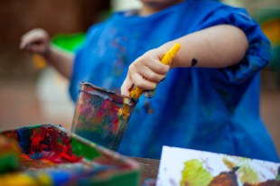 Child in blue top with container of paint