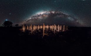A milkway shot against a landscape with metal structures like satellites.