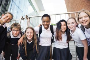 A group of seven happy high school students linking arms and posing for a group photo outside a museum.