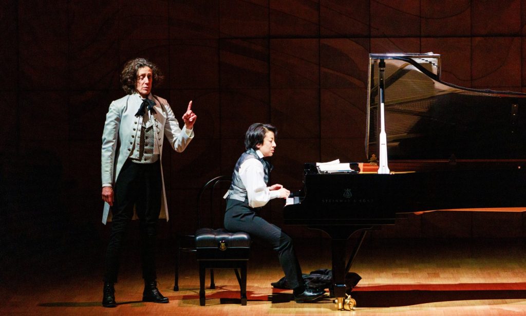 Pianist Aura Go, dressed as Chopin, is seated at the piano while actor Jennifer Vuletic, as composer Franz Liszt, stands behind.