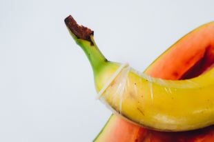 A banana with a condom and a sliced papaya underneath.