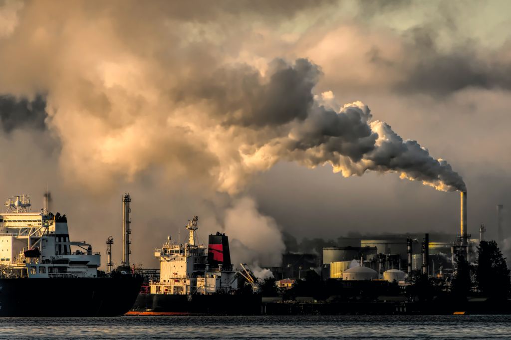 Factory chimneys belch smoke over a polluted industrial port.