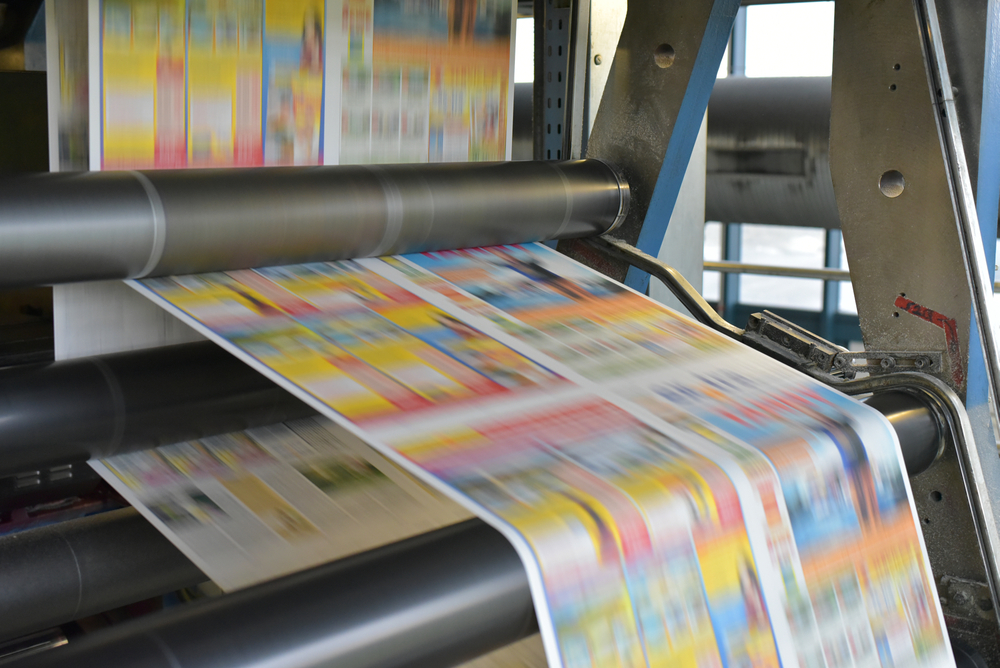 A brightly coloured newspaper front page being printed on a press. The image is blurred, indicating the speed at which the newspaper is printed.