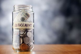 A glass jar half full of American coins and a few dollar notes labeled with the words "retirement" on it.