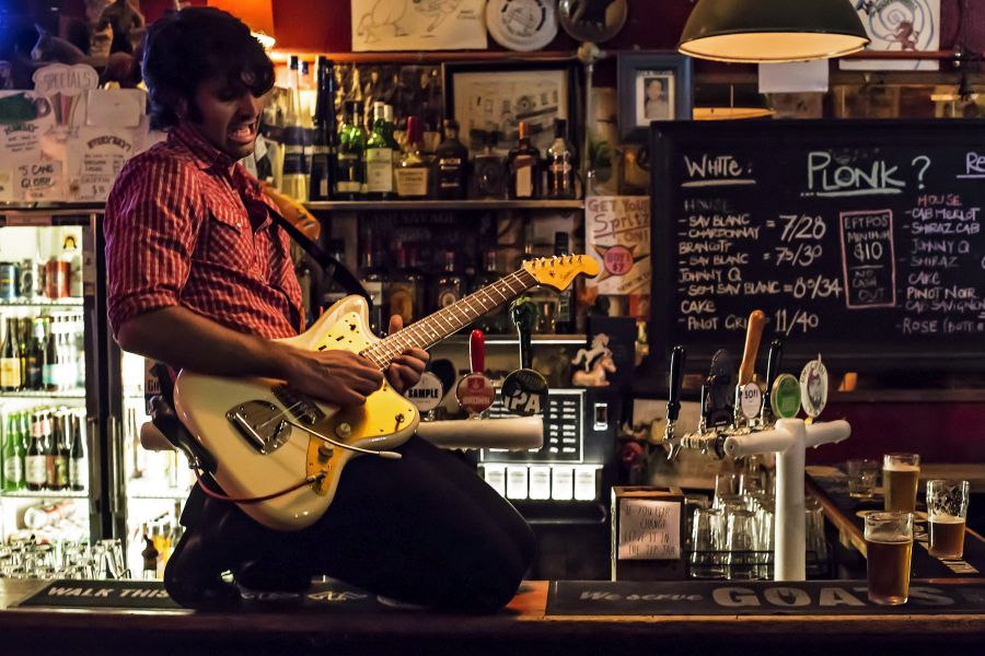 A young male guitarist playing an electric guitar skidding on his knees on the bar of a pub.