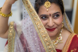 South Asian. Indian woman with red sari, gold jewellery and holding up a gold lined veil.