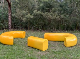 Carabiner Bench. Yellow coloured curved bench seating in parkland setting.