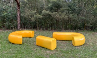 Carabiner Bench. Yellow coloured curved bench seating in parkland setting.
