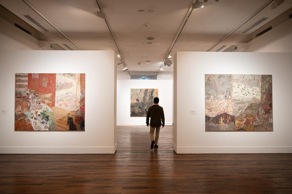 man walking in gallery with abstract paintings by artist Elisabeth Cummings