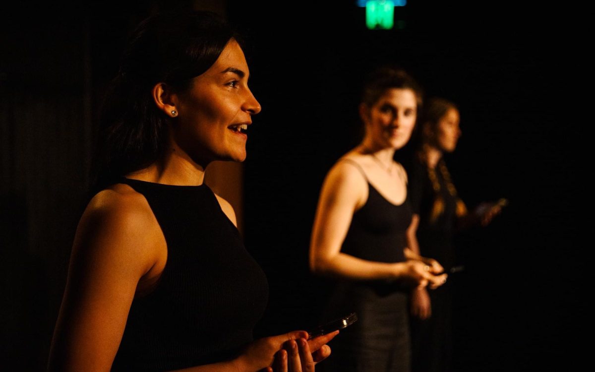 WAAPA’s Bachelor of Performing Arts (Honours). Two young woman are on stage performing and wearing sleeveless black tops. A third figure is in the background.