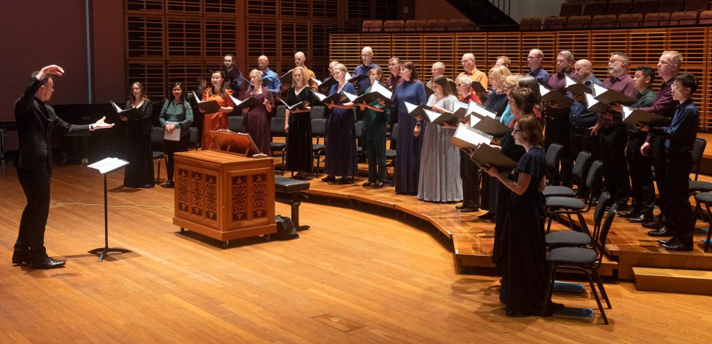 A conductor on the left conducting the Sydney Chamber Choir on the right.