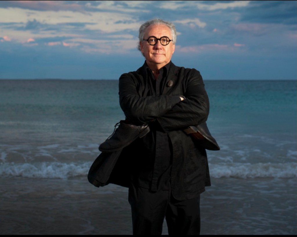 Vale Ted Snell. Man dressed in black standing on beach with arms crossed.