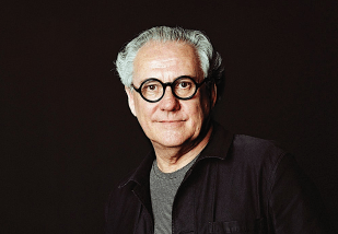 Vale Ted Snell. Creative looking elderly man with black glasses and photographed against a black background.