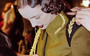 Fashion. Woman with slicked wavy hair is looking down at her khaki uniform style tunic, with gold braiding and epaulettes.