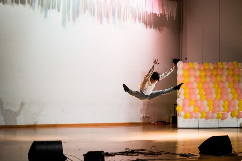 A male ballet dancer caught mid-leap in a dynamic rehearsal room photo.