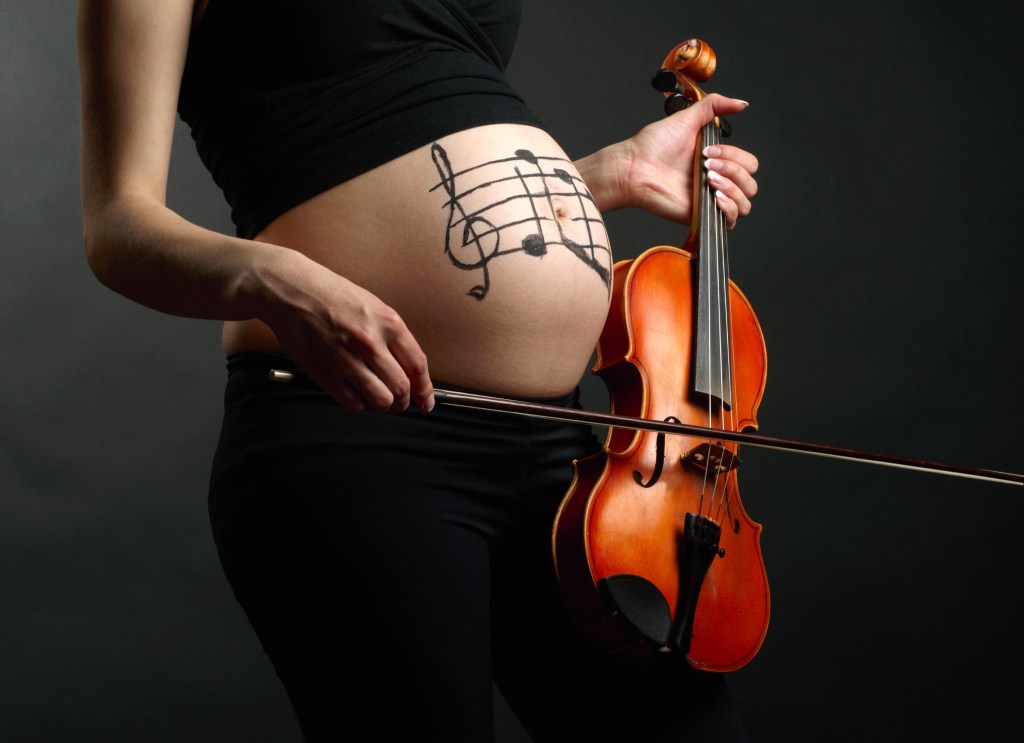 The torso of a pregnant violinist with musical notes drawn on the bare stomach.
