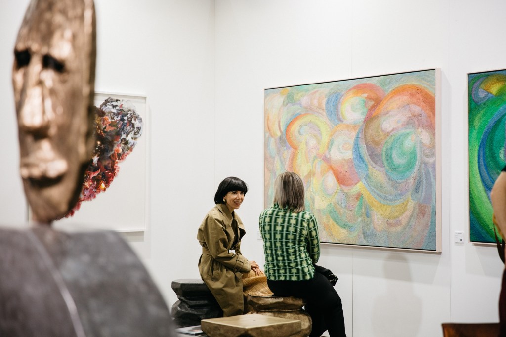 Melbourne Art Fair 2022. Photo: Marie-Luise Skibbe. Photo of two people sitting on a bench speaking about artworks on the walls in front of them.
