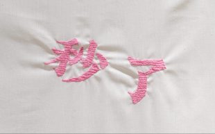 translation. image is of pink Indonesian text embroidered on a white background.