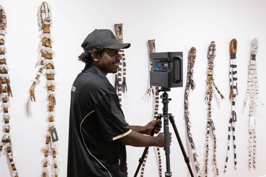 Aboriginal man holding photographic equipment in a gallery environment.