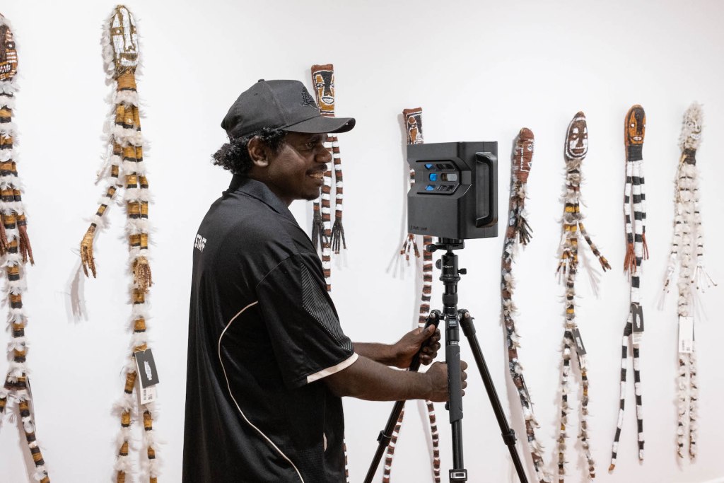 Aboriginal man holding photographic equipment in a gallery environment.