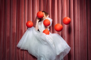 Bacon. Image is a woman in a white wedding-like dress trying to dodge six orange balls being thrown at her.