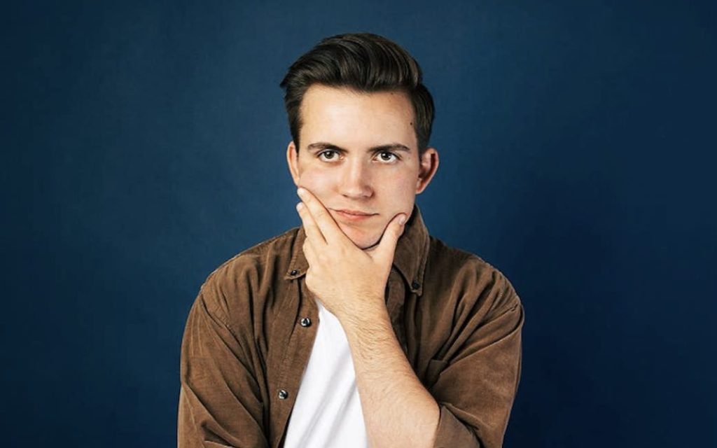 How to Shave. Image is of transman with brown shirt over white t-shirt stroking his chin