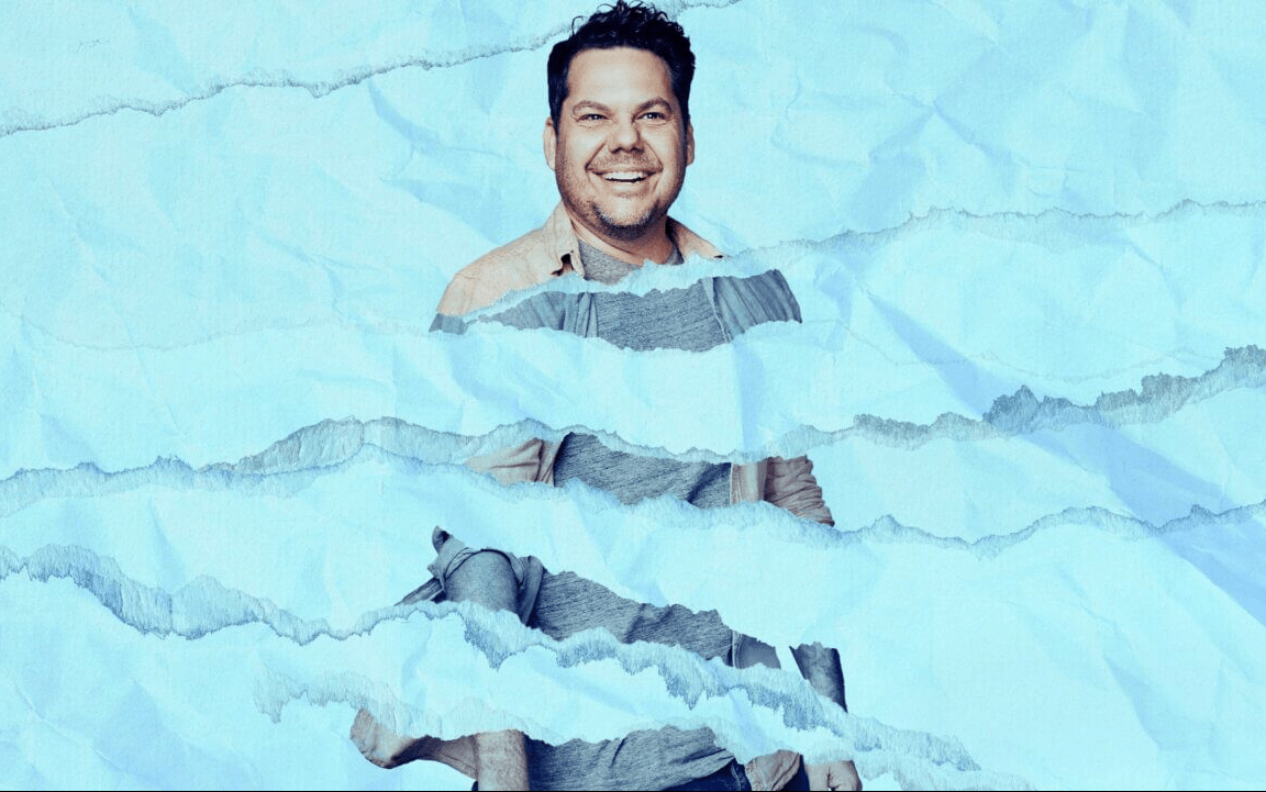 Every Brilliant Thing. Image is man behind blue swathes to make it look as if he's in a pool. He has a big smile on his face.
