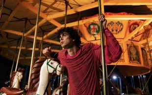 Image is of a man in a red shirt holding to the poles of a carousel. Gown by Kate V M Sylvester made from deconstructed t-shirt for We the Makers Sustainable Fashion Prize 2023. Image: Supplied.