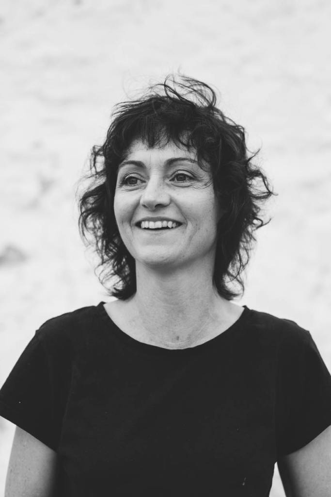 path. Image is a black and white head and shoulders shot of a woman looking off to the left, with shortish wavy hair and wearing a dark T-shirt. She is smiling.