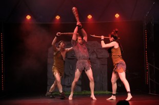 children's theatre. three performers on stage dressed as cave people attacking each other with clubs.