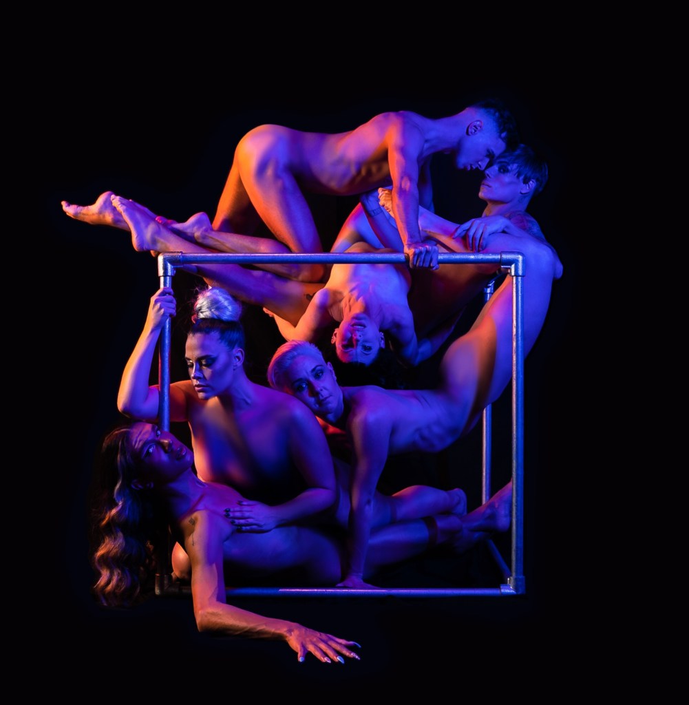 Tender. A tangle of naked bodies on a steel cube against a black background.