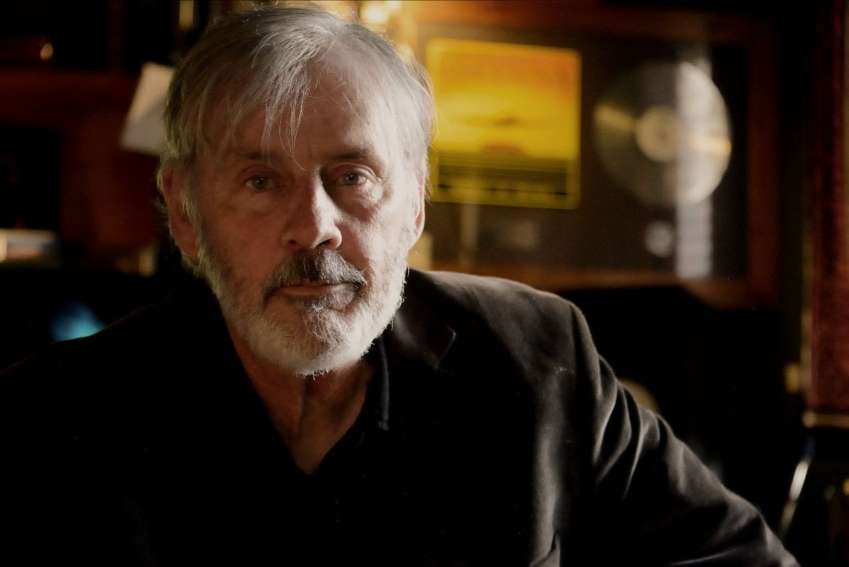 Howard. image is head and shoulders shot of middle-aged man with grey hair, beard and moustache, with a grave expression.