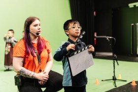 A primary student holds a clapper board at ACMI green-screen lab for kids.